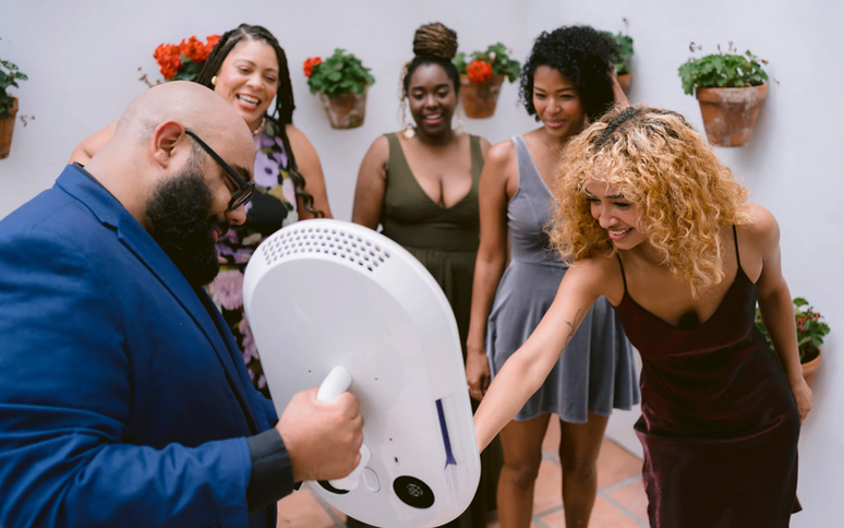 An attendant holding the portable photo booth out to a group of laughing guests at an outdoor party